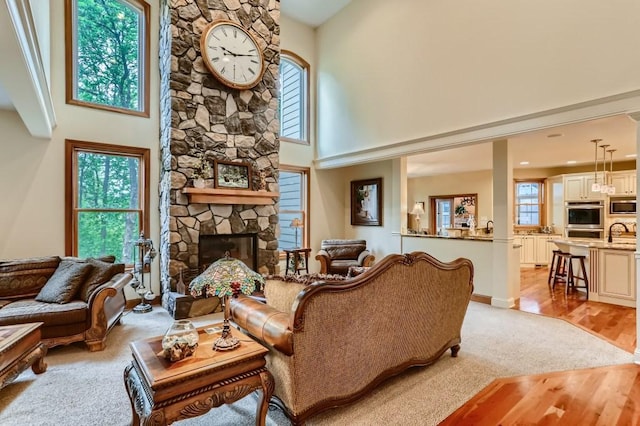 living room with a stone fireplace, a wealth of natural light, light hardwood / wood-style flooring, and a high ceiling