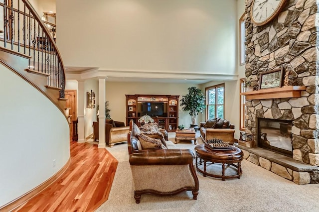 living room featuring a stone fireplace, wood-type flooring, and a towering ceiling