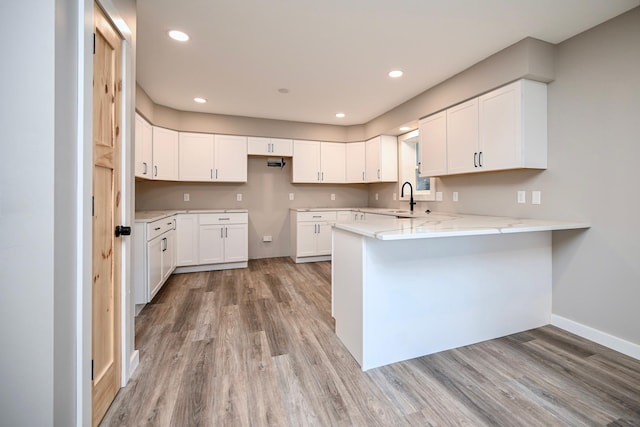 kitchen featuring white cabinets, light wood-type flooring, kitchen peninsula, and sink