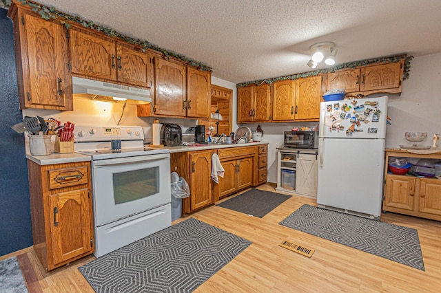 kitchen with a textured ceiling, white appliances, and light wood-type flooring