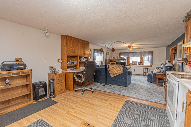 home office featuring ceiling fan, light hardwood / wood-style flooring, and a textured ceiling