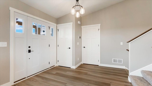 foyer entrance featuring wood-type flooring, lofted ceiling, and a chandelier