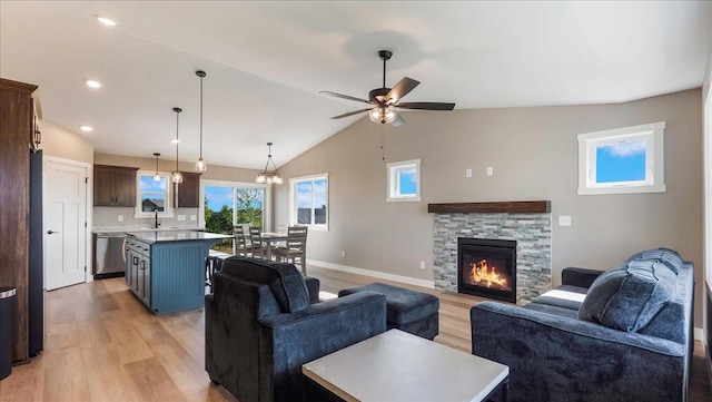 living room featuring ceiling fan, sink, a stone fireplace, light hardwood / wood-style floors, and lofted ceiling