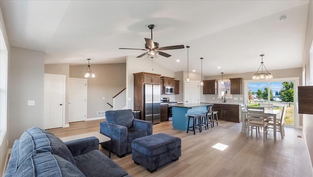 living room with sink, ceiling fan with notable chandelier, vaulted ceiling, and light wood-type flooring