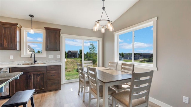 dining space with light hardwood / wood-style floors, an inviting chandelier, lofted ceiling, and sink