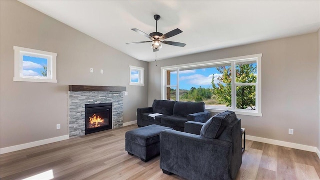 living room featuring light wood-type flooring, a stone fireplace, ceiling fan, and vaulted ceiling