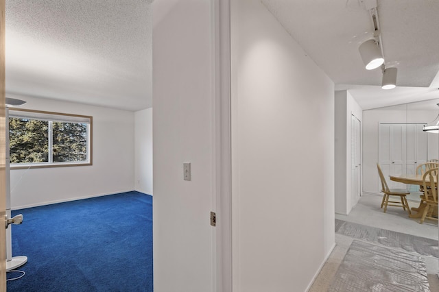 hallway with carpet flooring, a textured ceiling, and vaulted ceiling