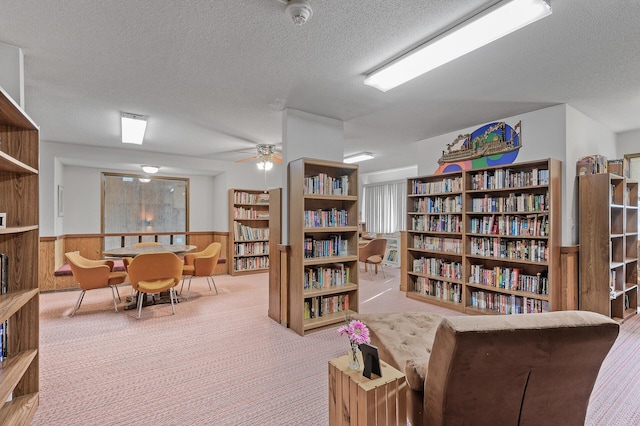 sitting room featuring ceiling fan, wood walls, a textured ceiling, and light carpet