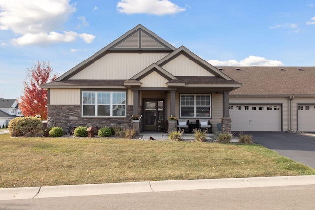 craftsman house featuring an attached garage, driveway, a front lawn, and stone siding