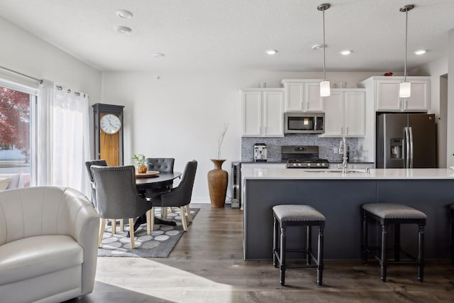 kitchen with stainless steel appliances, white cabinetry, light countertops, backsplash, and decorative light fixtures