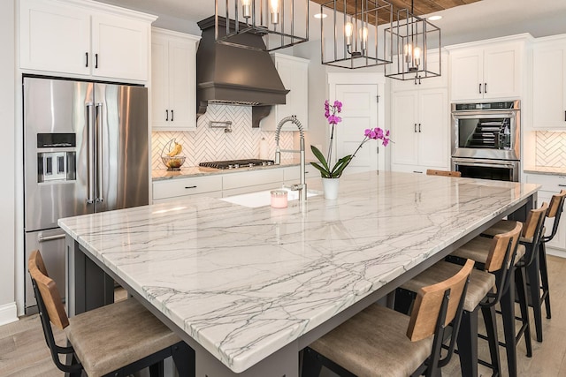 kitchen with a large island with sink, stainless steel appliances, light hardwood / wood-style flooring, and white cabinetry