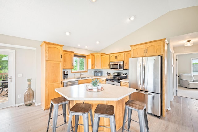 kitchen with stainless steel appliances, a kitchen island, a kitchen breakfast bar, and light hardwood / wood-style floors