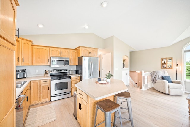 kitchen with lofted ceiling, a kitchen bar, light hardwood / wood-style flooring, a kitchen island, and appliances with stainless steel finishes