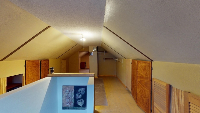 bonus room featuring vaulted ceiling, a textured ceiling, and light wood-type flooring