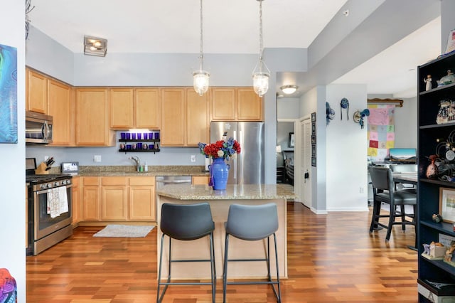 kitchen featuring light stone countertops, light brown cabinets, stainless steel appliances, and hardwood / wood-style flooring