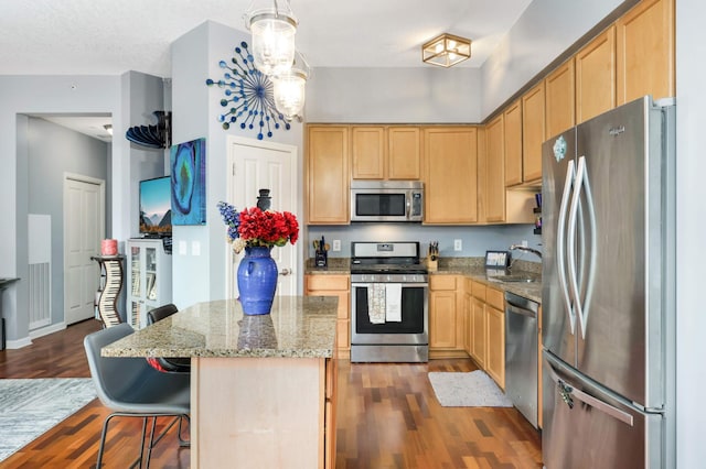 kitchen featuring light brown cabinets, sink, appliances with stainless steel finishes, decorative light fixtures, and a kitchen island