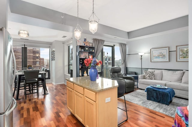 kitchen featuring light brown cabinets, dark hardwood / wood-style floors, light stone countertops, a kitchen island, and stainless steel refrigerator