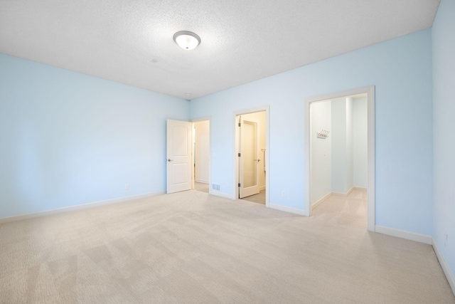 unfurnished bedroom with ensuite bath, light carpet, and a textured ceiling