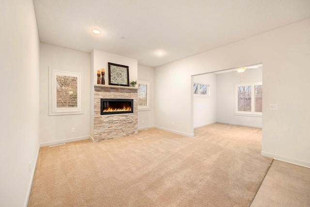 unfurnished living room with a stone fireplace, recessed lighting, baseboards, and light carpet