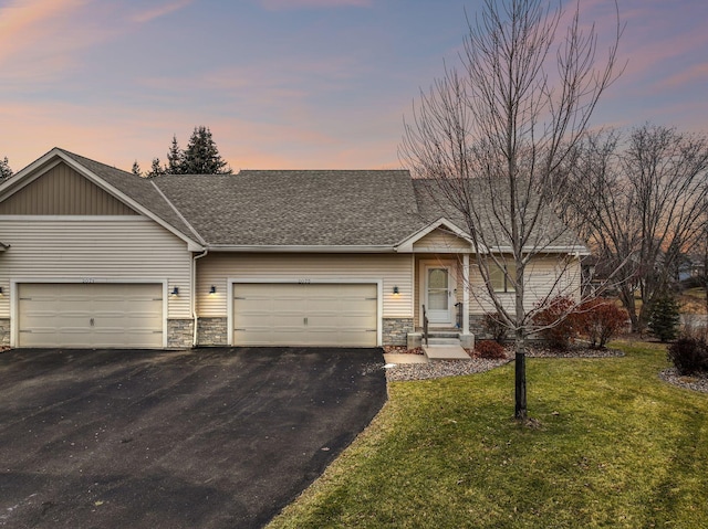 view of front of house with stone siding, driveway, a front lawn, and roof with shingles