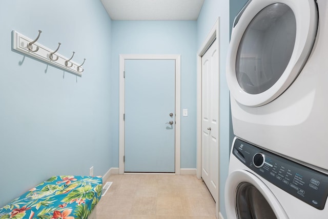 clothes washing area featuring laundry area, visible vents, stacked washer and clothes dryer, and baseboards