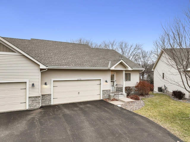 view of front of property featuring aphalt driveway, stone siding, roof with shingles, a front yard, and a garage