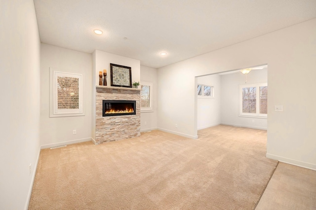 unfurnished living room featuring carpet flooring, baseboards, and a stone fireplace