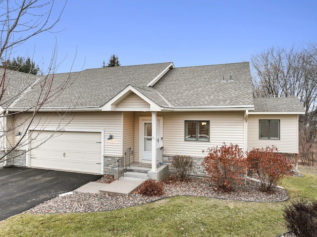 ranch-style home featuring driveway, roof with shingles, a front lawn, an attached garage, and stone siding