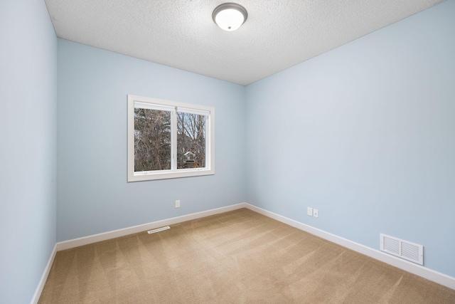 carpeted empty room featuring a textured ceiling, baseboards, and visible vents
