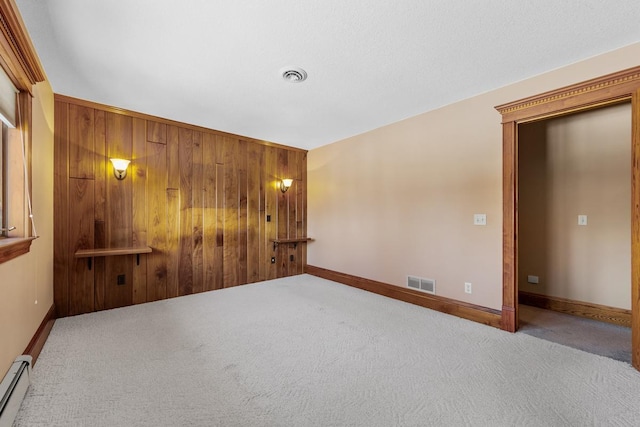 spare room with wood walls, carpet floors, and a baseboard heating unit