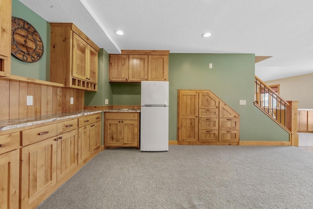 kitchen featuring light carpet, white fridge, light stone counters, and a textured ceiling