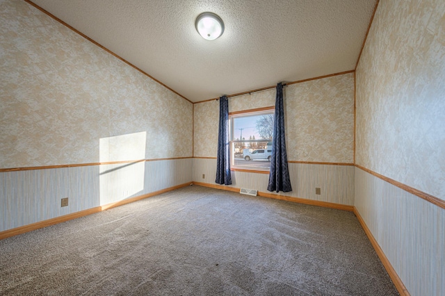 carpeted empty room with vaulted ceiling, ornamental molding, and a textured ceiling