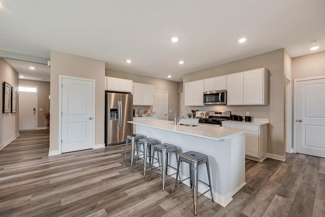 kitchen with white cabinets, appliances with stainless steel finishes, a center island with sink, and hardwood / wood-style floors