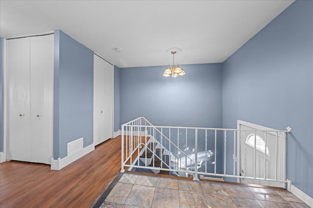 interior space featuring an inviting chandelier, wood finished floors, visible vents, an upstairs landing, and baseboards
