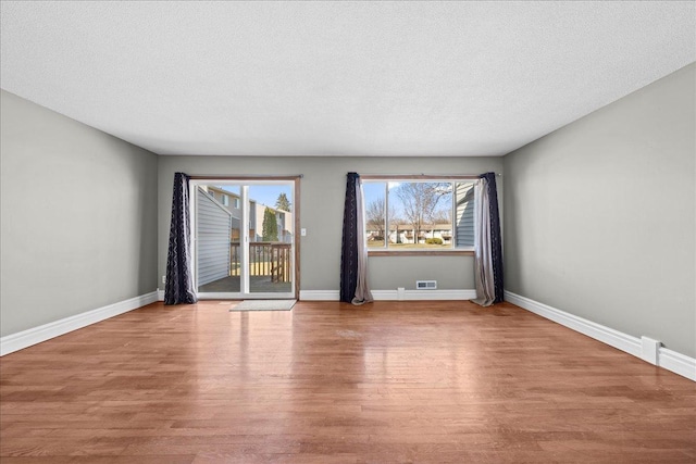 spare room featuring baseboards, wood finished floors, visible vents, and a textured ceiling