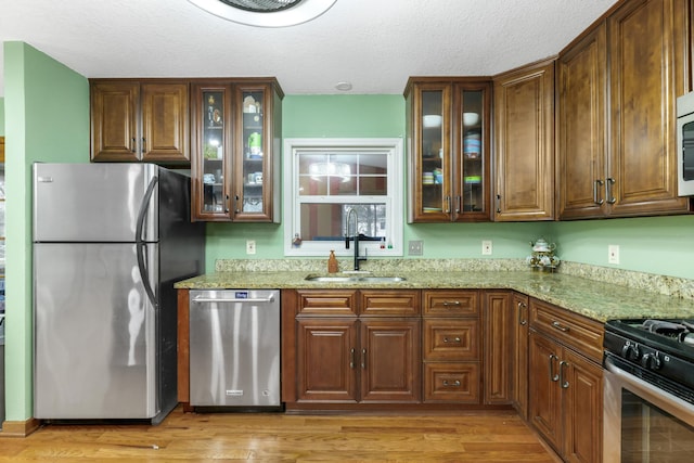 kitchen featuring appliances with stainless steel finishes, sink, light stone countertops, a textured ceiling, and light hardwood / wood-style flooring