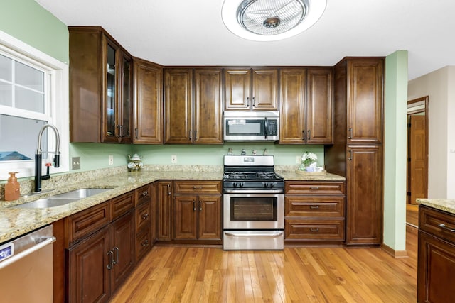 kitchen with sink, stainless steel appliances, light stone countertops, dark brown cabinets, and light wood-type flooring