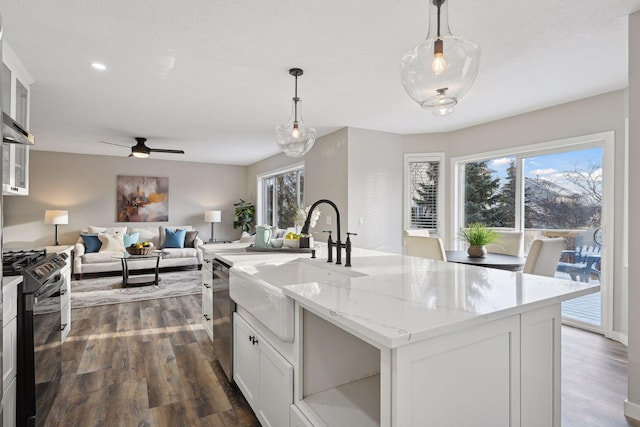 kitchen featuring a kitchen island with sink, dark wood-type flooring, decorative light fixtures, white cabinets, and black gas stove