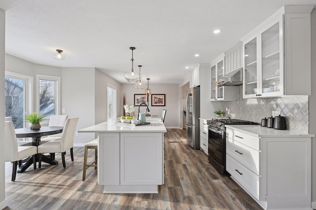 kitchen with stainless steel fridge, gas stove, dark wood-type flooring, pendant lighting, and an island with sink