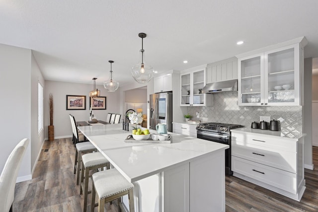 kitchen featuring stainless steel appliances, extractor fan, decorative light fixtures, a kitchen island with sink, and white cabinets