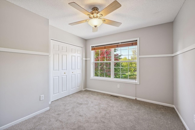 unfurnished bedroom featuring ceiling fan, a closet, light colored carpet, and a textured ceiling