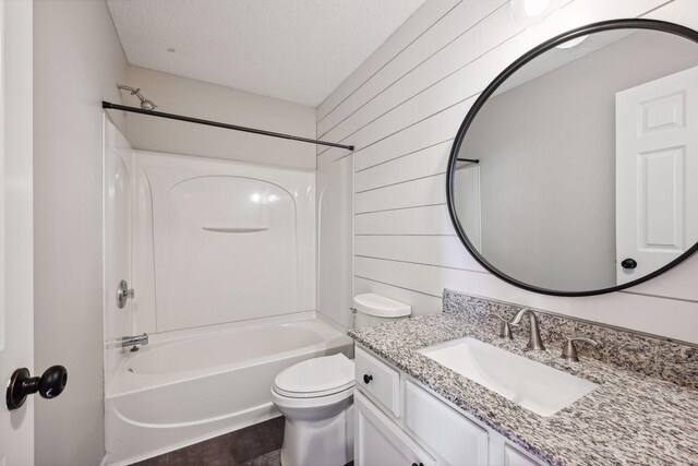 full bathroom with vanity, a textured ceiling, wooden walls, washtub / shower combination, and toilet