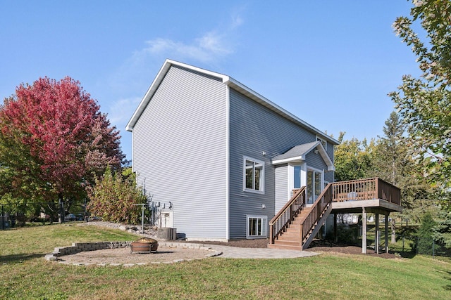 back of house with central AC unit, a fire pit, a lawn, and a wooden deck