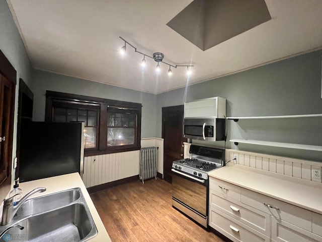 kitchen featuring hardwood / wood-style floors, radiator, sink, white cabinetry, and stainless steel appliances