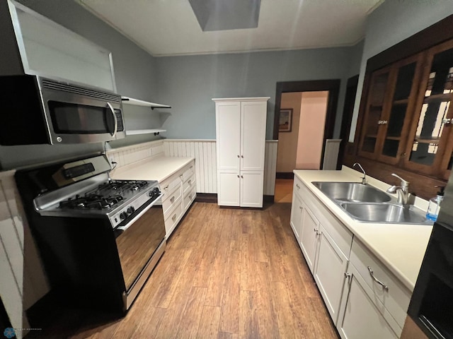 kitchen featuring light wood-type flooring, gas stove, white cabinetry, and sink