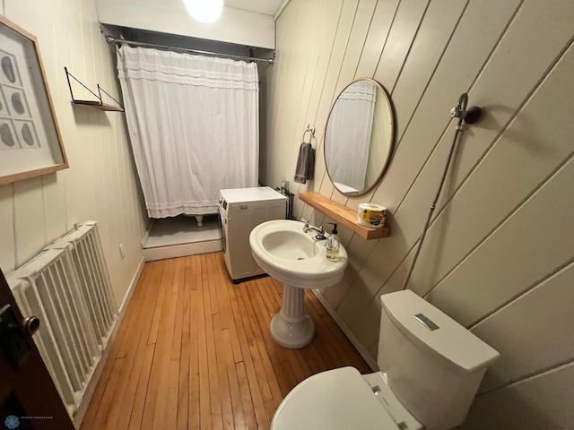 bathroom with radiator heating unit, wooden walls, hardwood / wood-style floors, and toilet