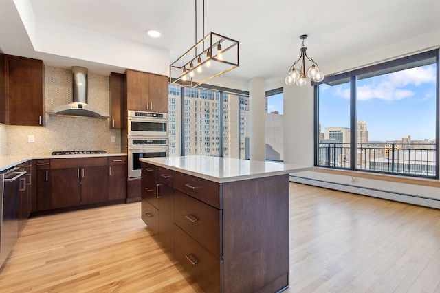 kitchen with light wood-type flooring, backsplash, stainless steel appliances, wall chimney range hood, and a kitchen island