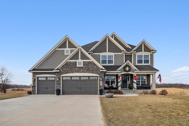 craftsman house featuring a garage, stone siding, a front yard, and driveway