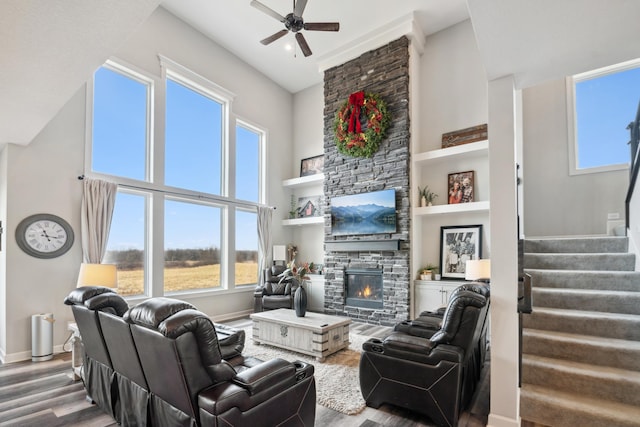 living area featuring baseboards, stairs, a stone fireplace, a high ceiling, and wood finished floors