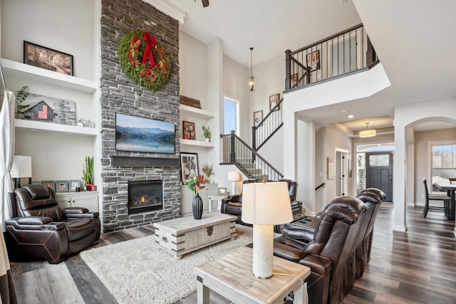 living room featuring baseboards, stairway, a stone fireplace, a towering ceiling, and wood finished floors